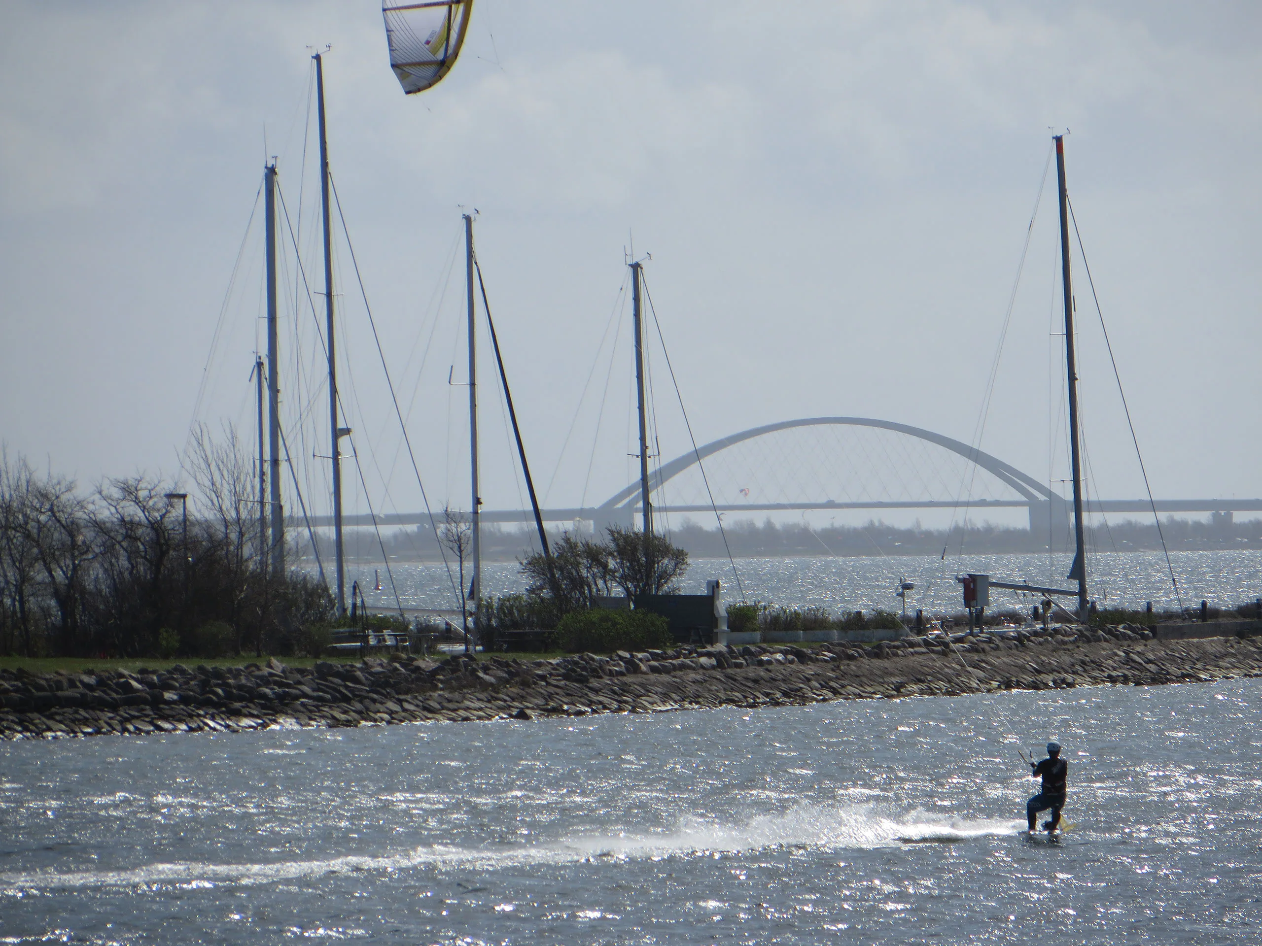 Kitesurfer vor Segelmasten und der Fehmarnsundbrücke