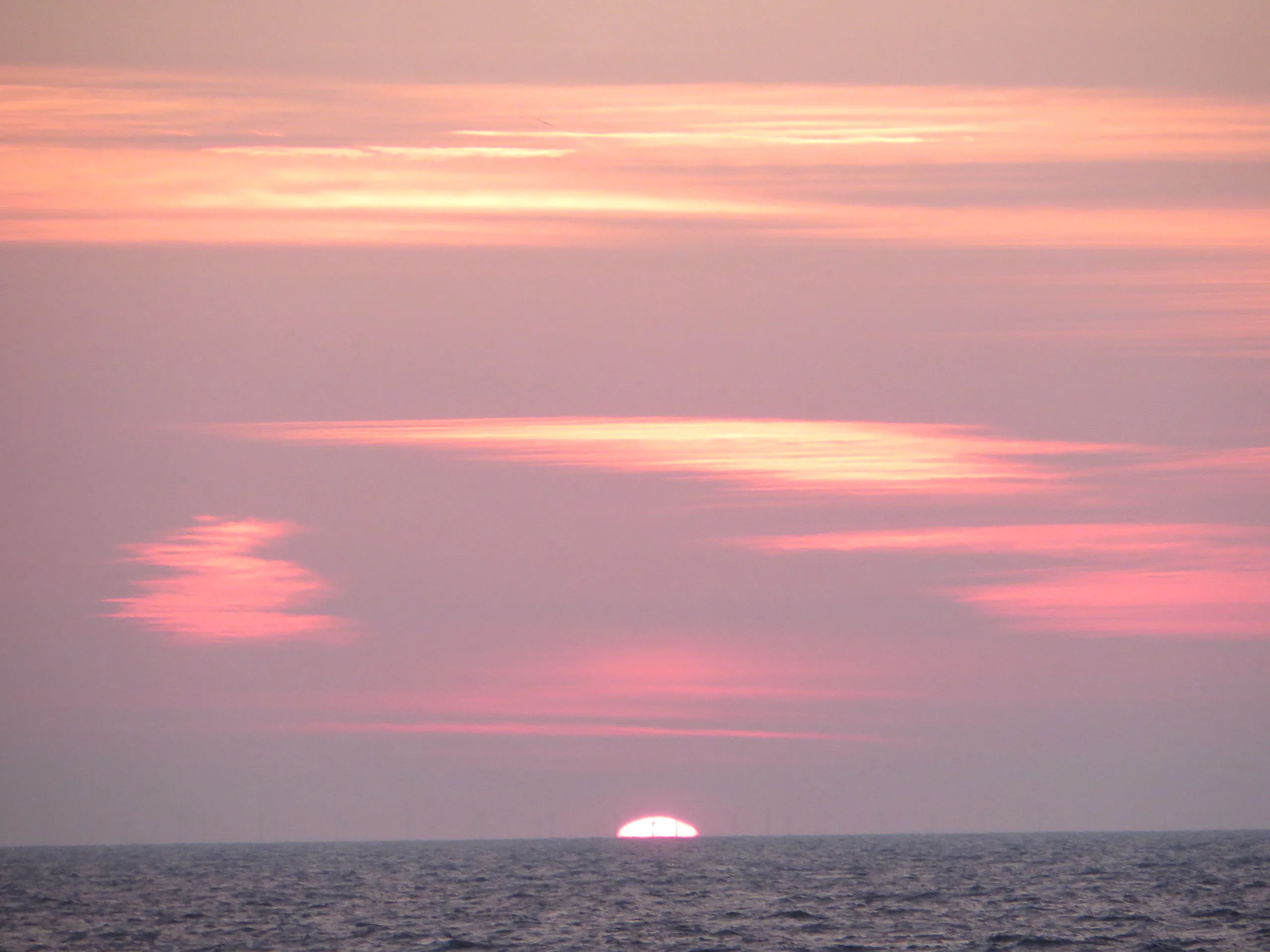 Tief stehende Sonne unter rosafarbenen Wolken über der Ostsee