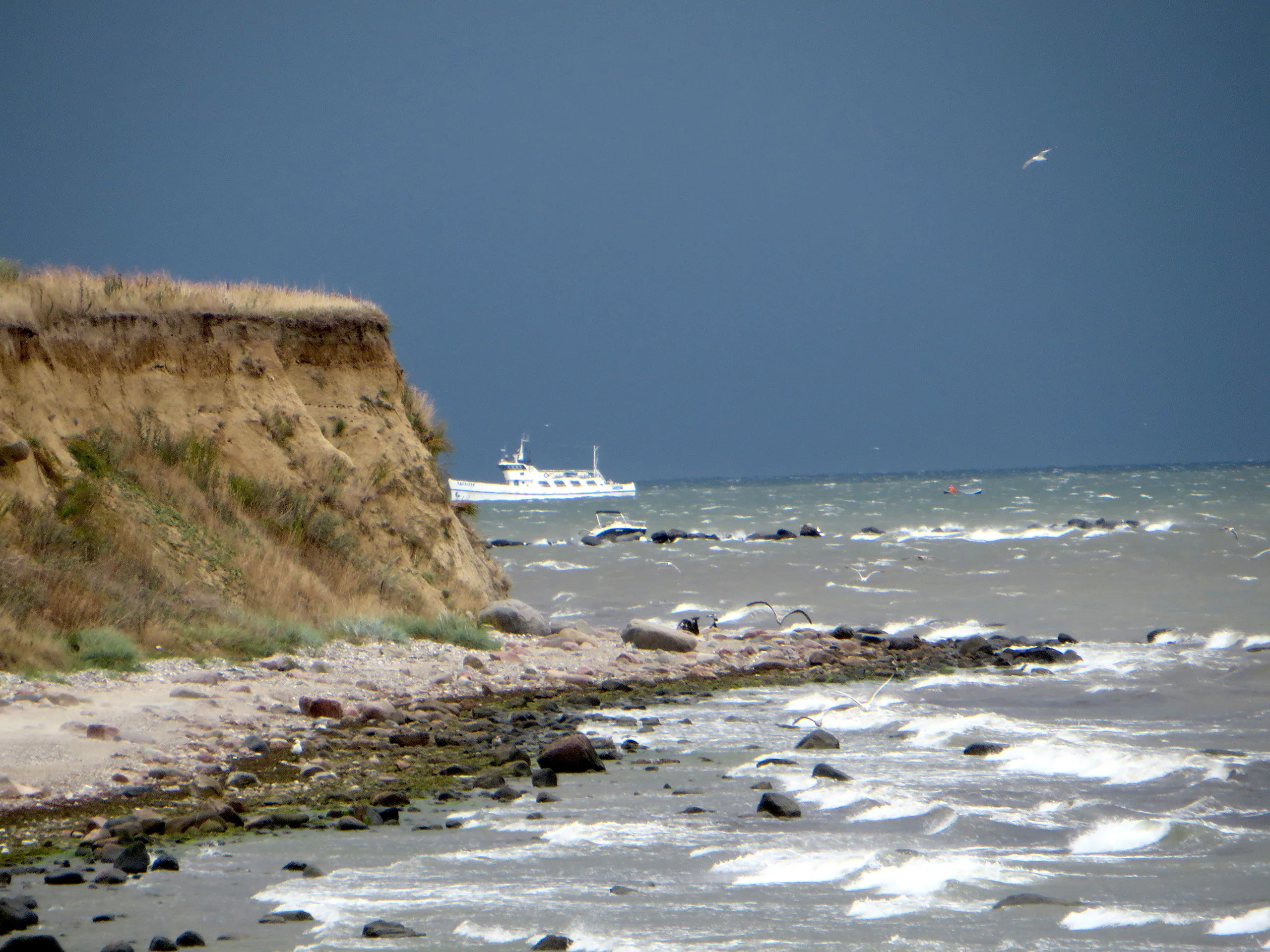 Steilküste mit Brandung und Ausflugsschiff vor Fehmarn