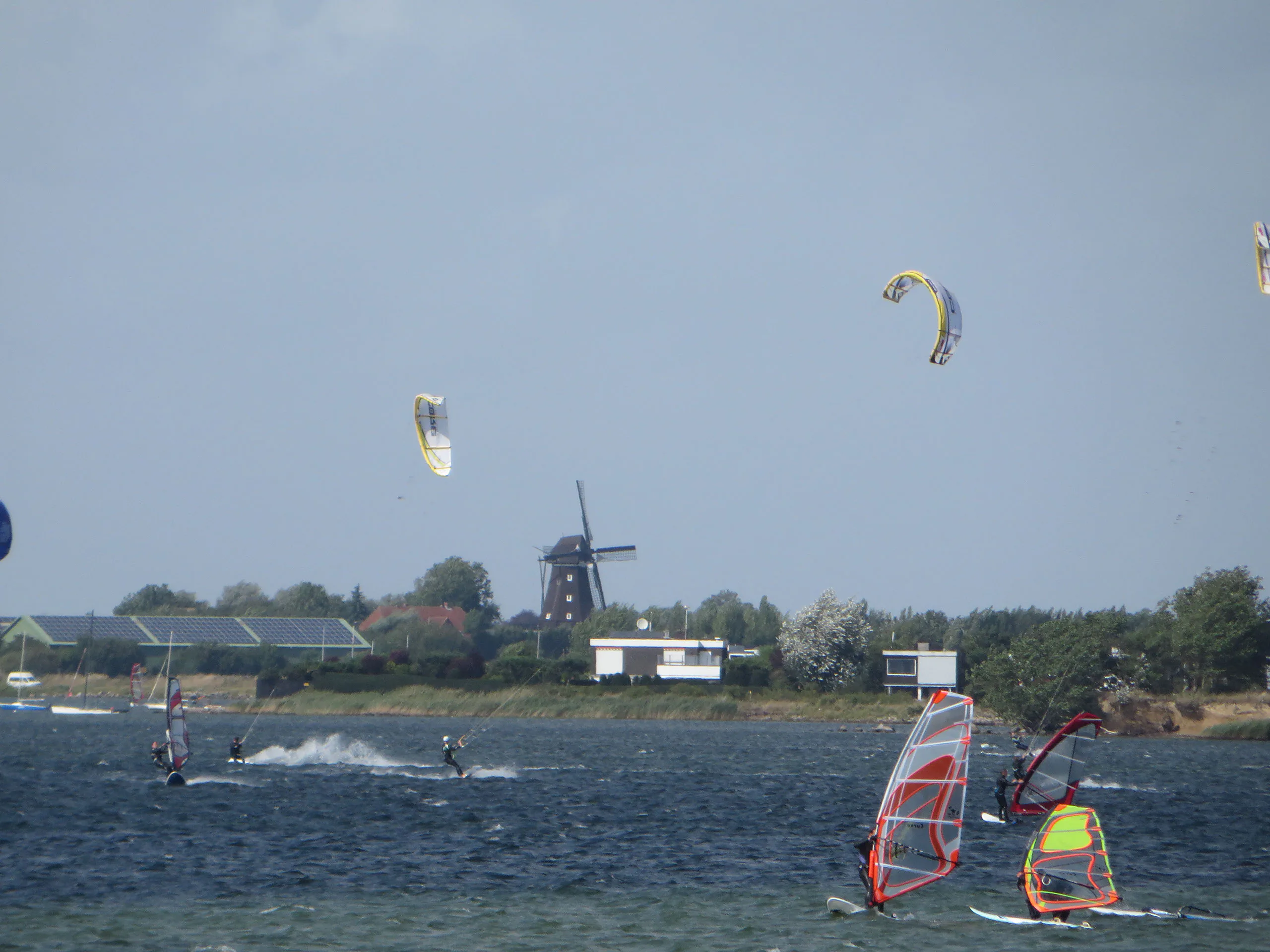 Kite- und Windsurfer vor einer Windmühle an Fehmarns Küste