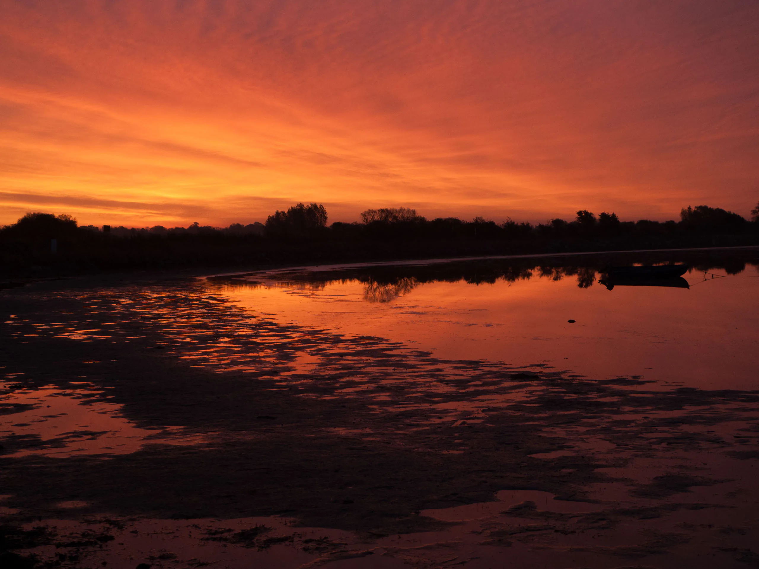 Orangefarbener Sonnenuntergang spiegelt sich in ruhigem Küstenwasser